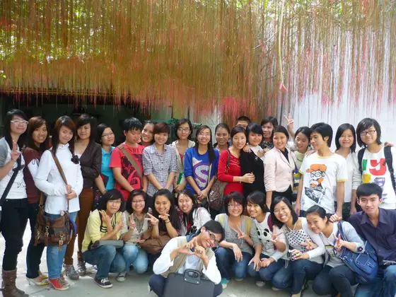 Nhóm đông người chụp ảnh dưới những dải trang trí nhiều màu treo dày, hàng trước ngồi thấp.