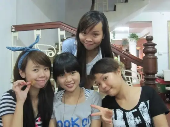 Bốn người tạo dáng trước cầu thang có tay vịn gỗ và lan can trắng, một người đeo băng đô xanh thắt nơ.